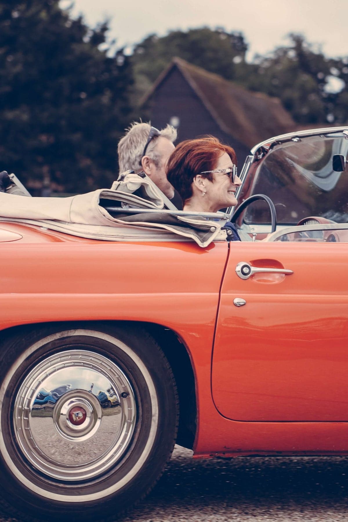 Älteres Paar fährt lachend gemeinsam in einem roten Oldtimer-Cabrio