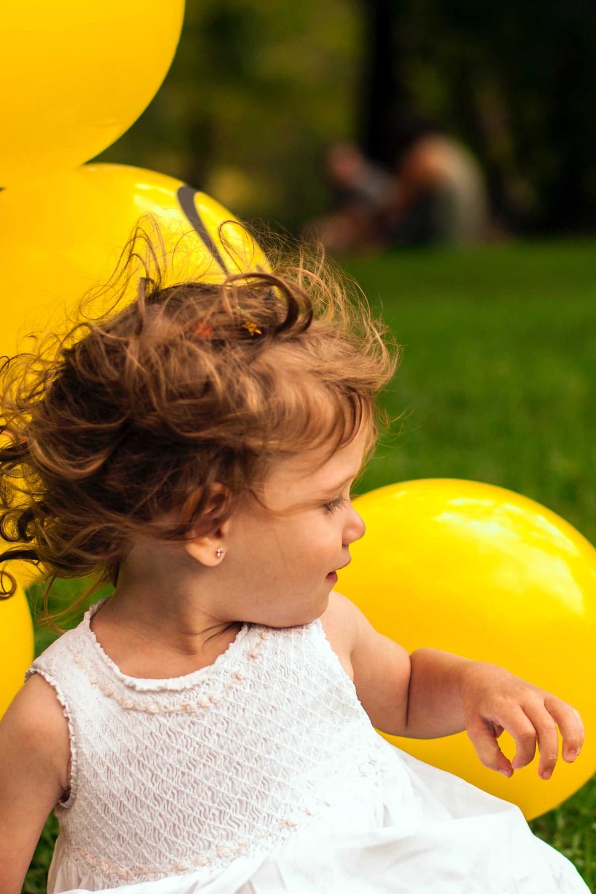 Kleines Mädchen im weißen Kleid spielt beim Willkommensfest mit gelben Luftballons